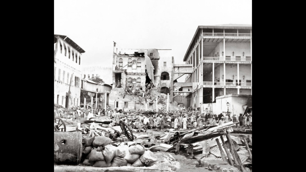 Wide view of a crowd gathered around the wreckage and collapsed buildings of the palace complex